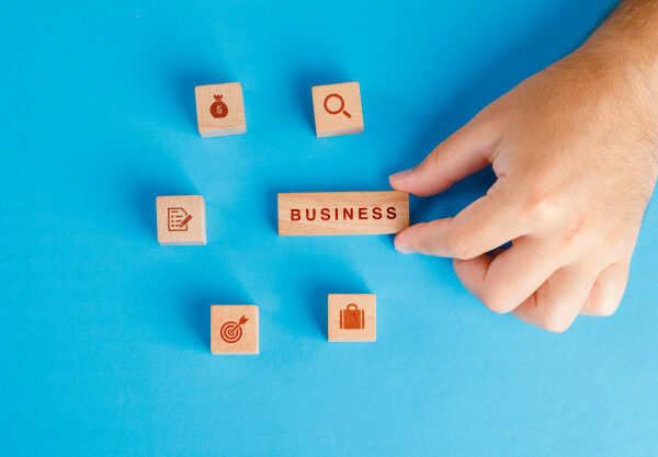 business-concept-with-icons-on-wooden-cubes-on-blue-table-flat-lay-hand-holding-wooden-block_176474-9353